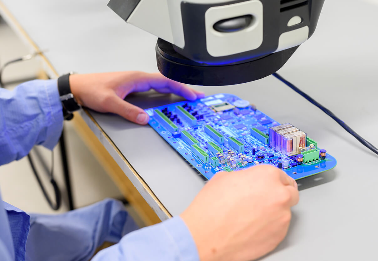 About Rapier Electronics Adelaide - Image of a worker checking a circuit board under a blue light.